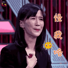 a woman in a black jacket is making a funny face while holding a red object in her hand .