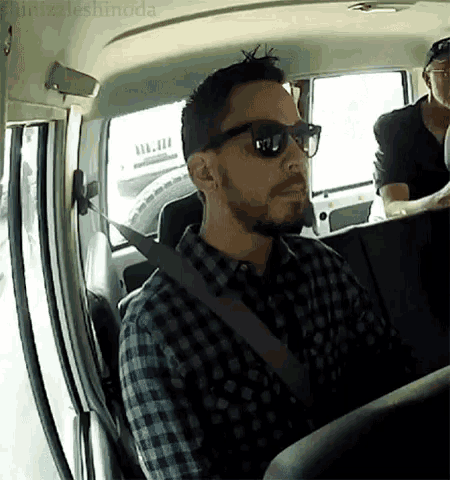 a man wearing sunglasses and a plaid shirt is sitting in a car .