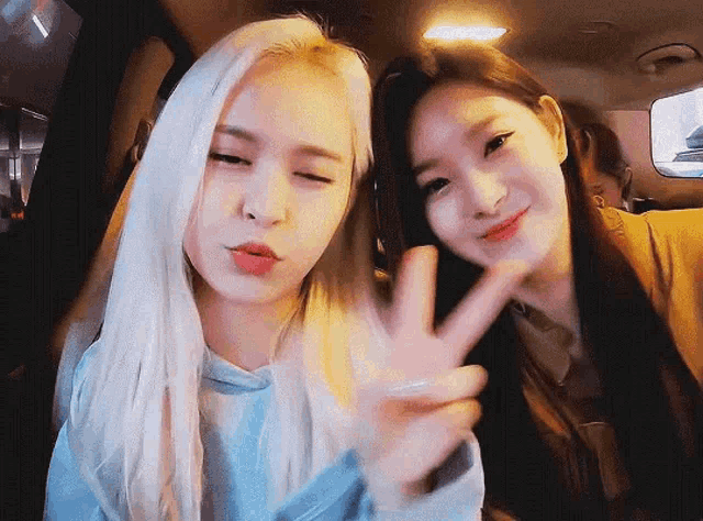 two young women are sitting in a car and making a peace sign .