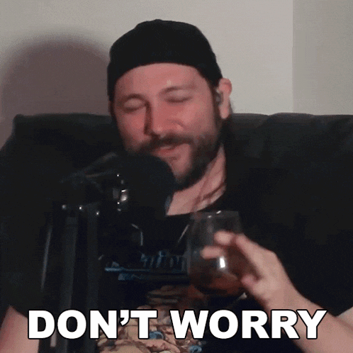 a man sitting in front of a microphone with a glass of wine and the words " don 't worry " above him