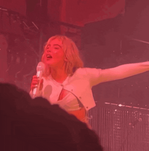 a woman singing into a microphone with her arms outstretched in front of a crowd