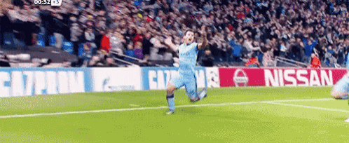 a soccer player is celebrating a goal on a soccer field in front of a nissan ad .