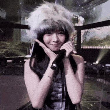 a woman wearing a fur hat is holding a microphone and making a funny face .