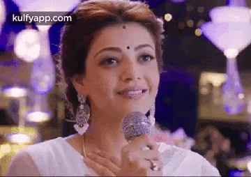 a woman in a white dress is holding a microphone in her hand and smiling .