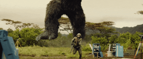 a man in a helmet stands in front of a giant gorilla in a field
