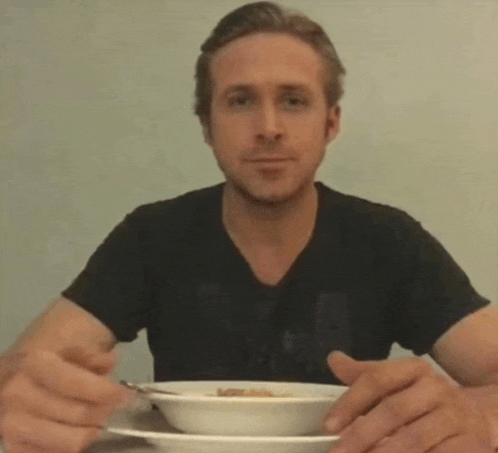 a man in a black shirt is sitting at a table eating a bowl of food