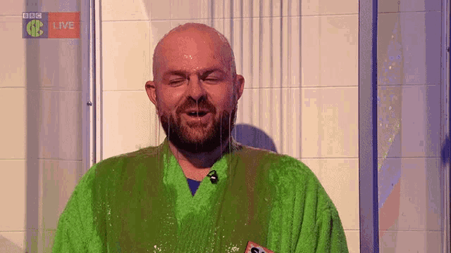 a man in a green robe is under a shower with bbc live in the corner