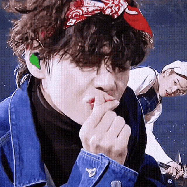 a close up of a person wearing a bandana and a denim jacket eating something .
