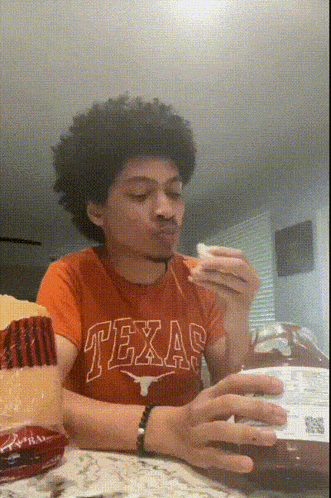 a young man wearing a texas shirt is eating a sandwich