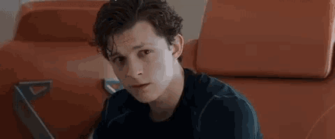a young man in a black shirt is sitting in an orange chair .