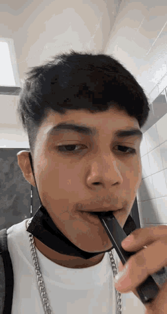 a young man wearing a black mask and a white shirt is smoking an electronic cigarette