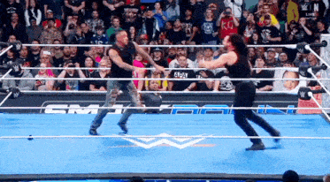 two men are wrestling in a ring with a crowd watching and one has a kc shirt on