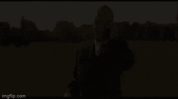 a man in a suit and tie is talking on a cell phone while standing in a field .
