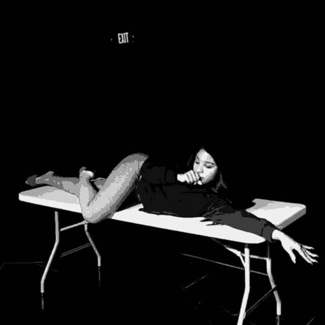 a woman is laying on a table with an exit sign in the background