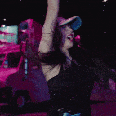 a woman in a black dress and a blue hat is dancing in front of a pink van