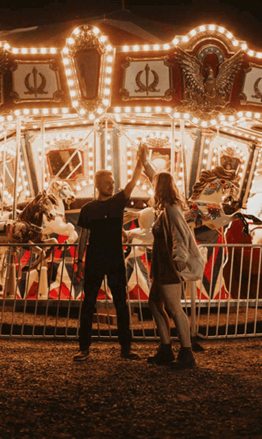 a man and a woman high five in front of a merry go round