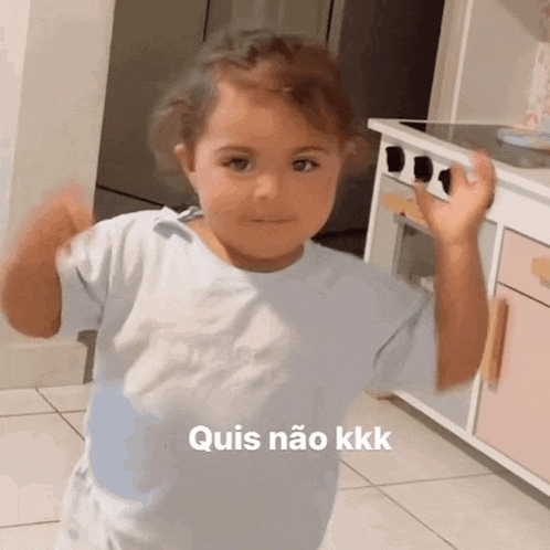 a little girl in a white shirt is standing in a kitchen with the words quis não kkk written on the bottom