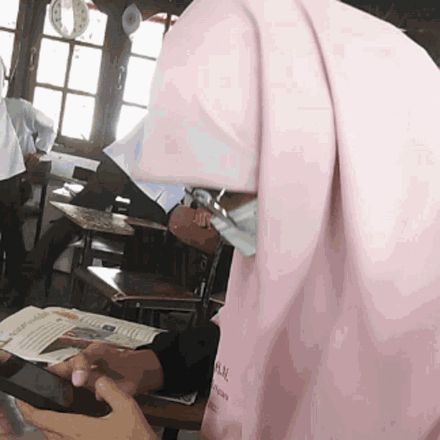 a girl wearing a pink hijab is sitting at a desk with a book