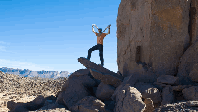 a man standing on top of a large rock with his arms in the air
