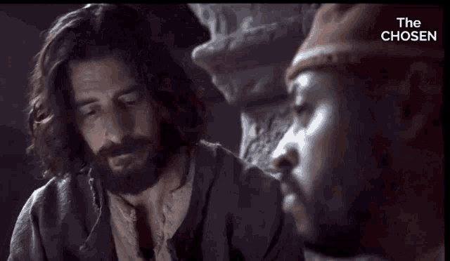 a man with long hair and a beard is talking to another man with the words the chosen below him