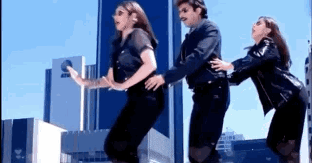 a man and two women are dancing in front of a tall building in a city .