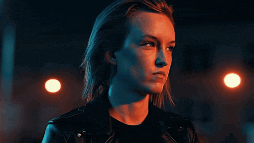 a woman wearing a black leather jacket stands in front of a building at night