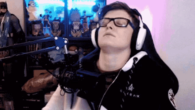 a man wearing headphones and glasses is sitting in front of a microphone with his eyes closed