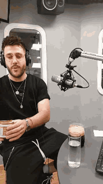 a man wearing headphones sits in front of a microphone holding a can of food