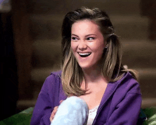 a woman in a purple hoodie is sitting on a couch laughing .