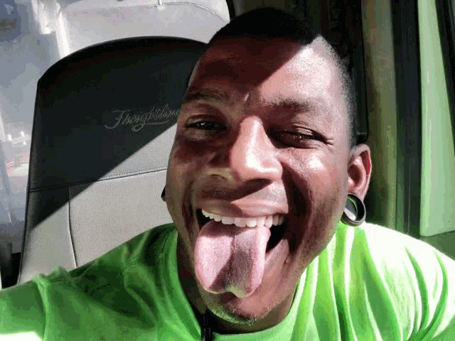 a man in a green shirt is sticking his tongue out in front of a seat that says freightliner