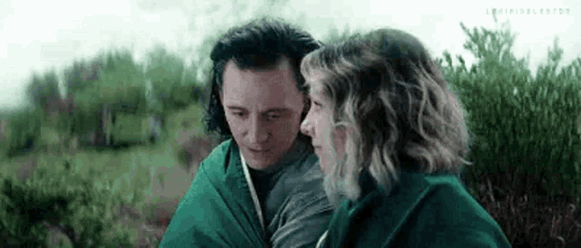 a man and a woman are wrapped in a green blanket and hugging each other .