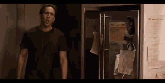 a man in a black shirt is standing in front of a refrigerator in a dark room .