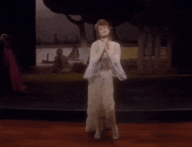 a woman in a white dress is dancing on a stage with trees in the background