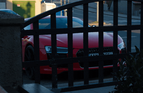a red car is parked behind a black fence and has a license plate that says aaw on it
