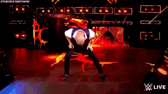 a man in a purple vest is dancing on a stage in front of a fire .