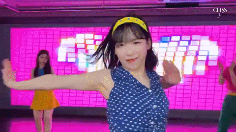 a girl in a blue polka dot shirt is dancing in front of a pink background .