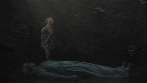 a woman in a dress is standing next to a man laying in the water