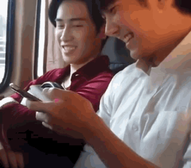 two young men are sitting next to each other in a car looking at their phones .