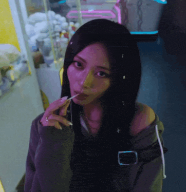 a woman with long black hair is eating a lollipop in front of a neon sign