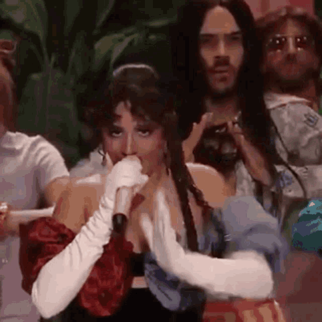 a woman wearing white gloves is singing into a microphone while a group of people watch .