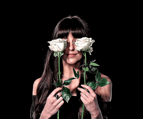a woman with long hair is holding two white roses in front of her eyes .