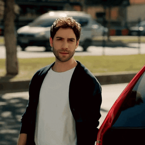 a man in a white shirt and black jacket is standing next to a car