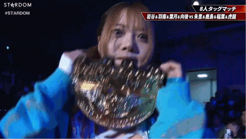 a woman wearing a blue shirt is holding a wrestling belt in front of her face