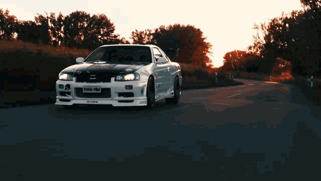 a white car with a license plate that says nism on it is driving down a road