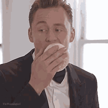 a man in a tuxedo and bow tie is eating a piece of bread .