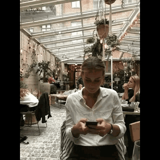a woman in a white shirt is looking at her phone in a restaurant