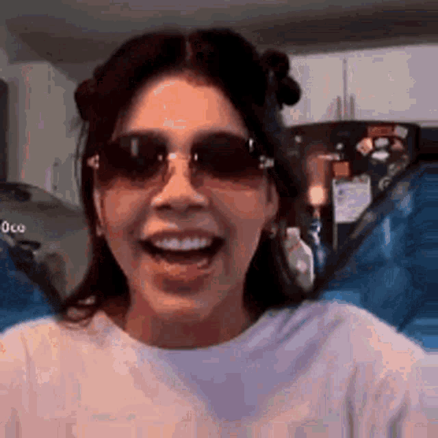 a woman wearing sunglasses and a white shirt is smiling in front of a refrigerator .