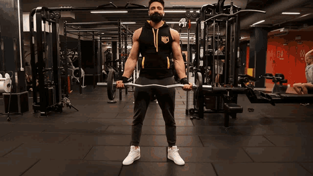a man with a beard is lifting a barbell in a gym with a hoodie that says kings on it