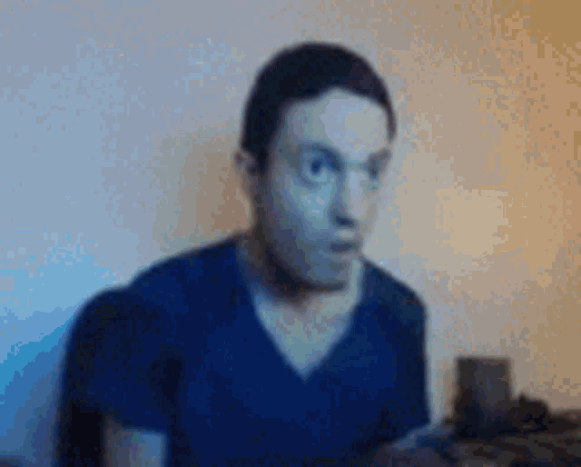a man in a blue shirt is sitting in front of a computer screen making a surprised face .
