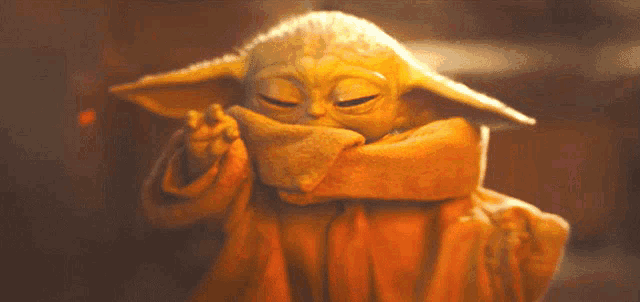 a close up of a baby yoda covering his face